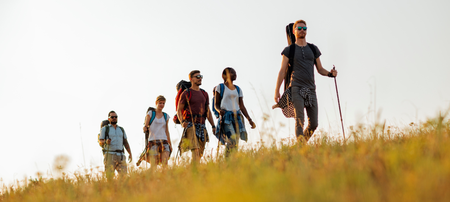 Gruppe von fünf Personen wander mit Rucksäcken über ein Feld.