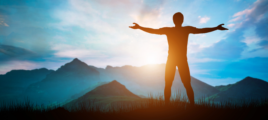 Person steht mit dem Rücken zum Betrachter auf einem Berg, im Hintergrund der Sonnenaufang.