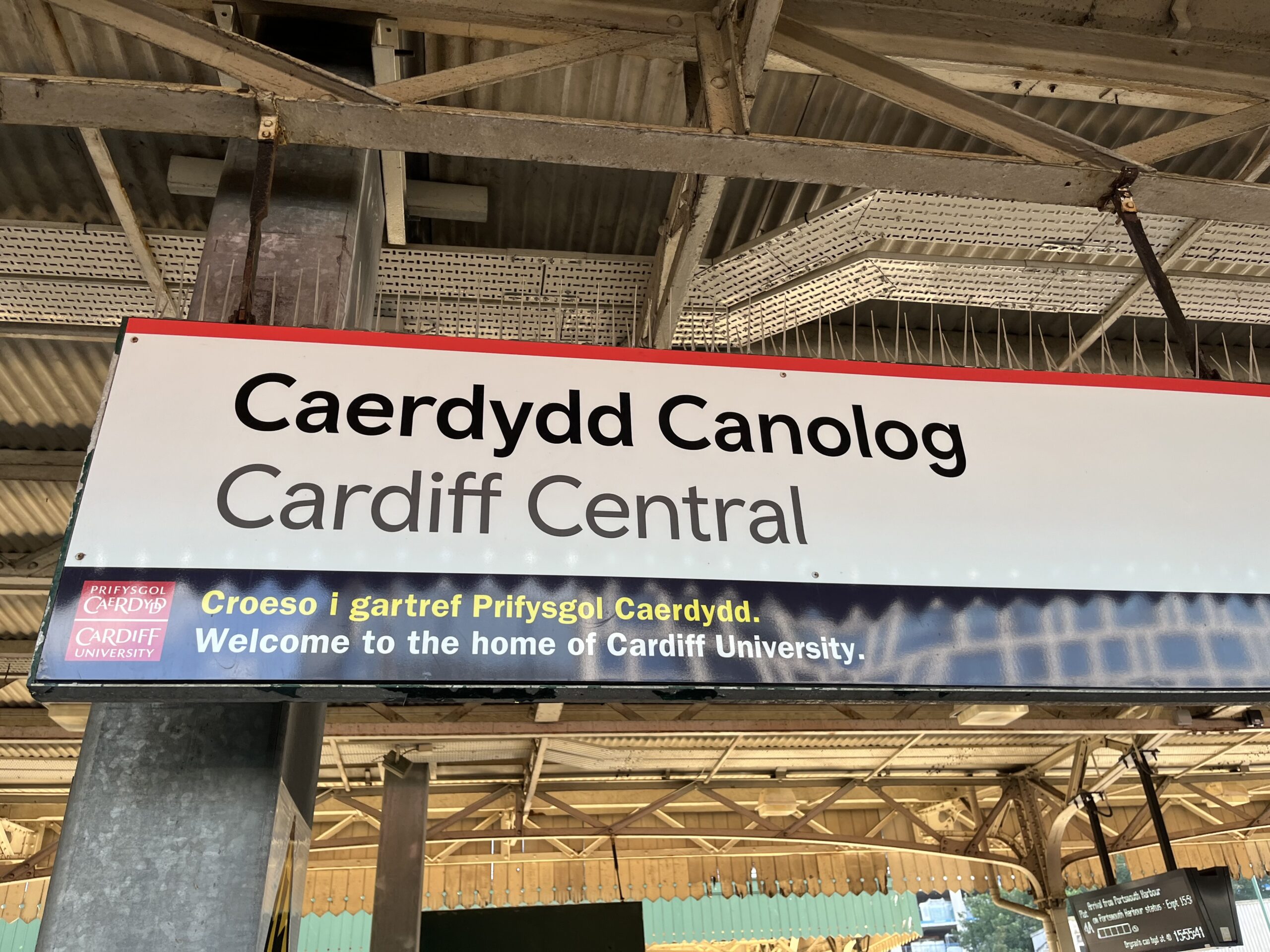 Bahnhofstafel mit der Aufschrift "Caerdydd Canolog - Cardiff Central. Welcome to the home of Cardiff University."