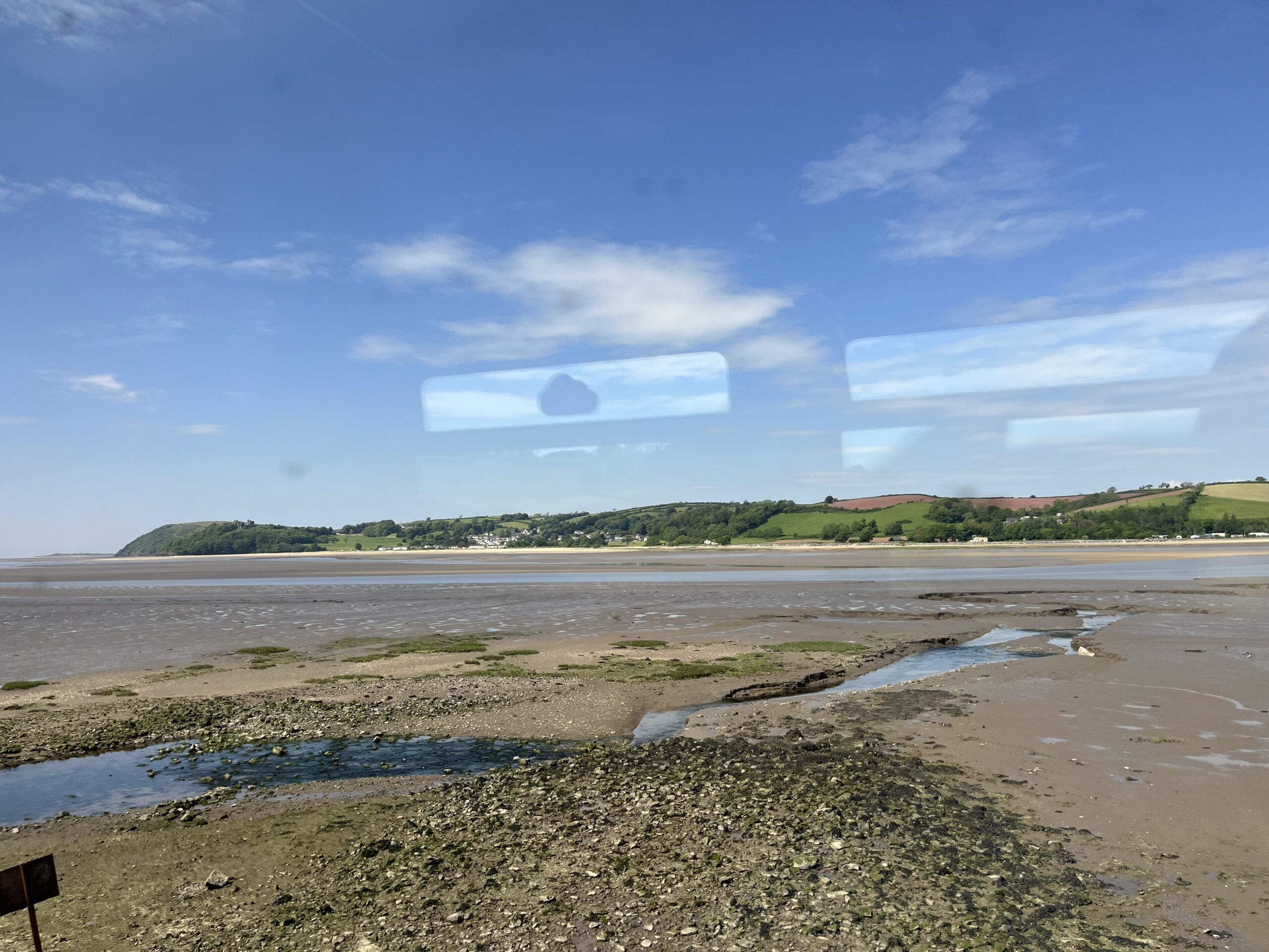 Blick aus dem fahrenden Zug auf einen Strand, grüne Hügel und den blauen Himmel.