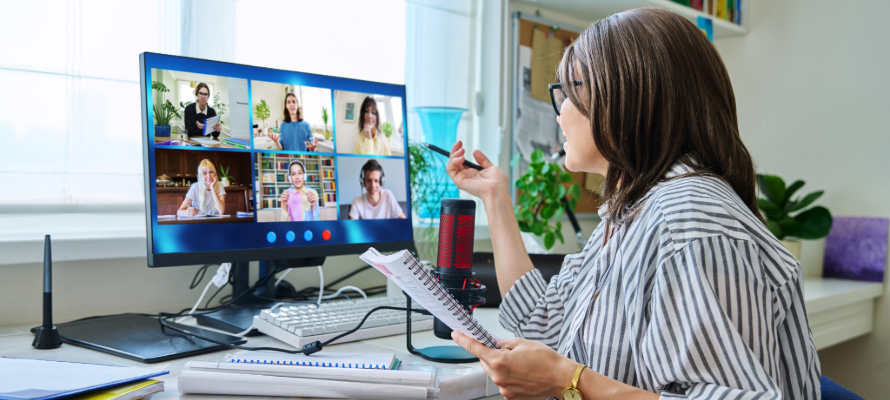 Frau sitz am Schreibtisch und nimmt an einem Online-Meeting teil, auf dem Bildschirm sind sechs weitere Personen zu sehen.