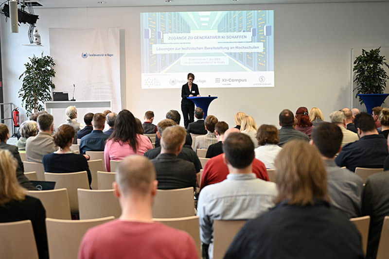 In einem großen Seminarraum nehmen TeilnehmerInnen an der Eröffnung des Symposiums "Zugänge zu generativen KI schaffen" teil.