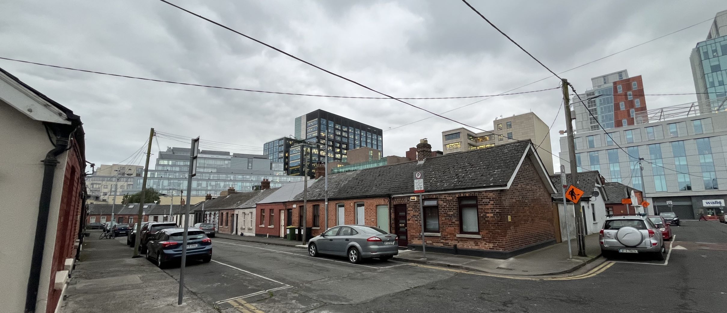 Blick auf eine bewohnte Straße in Dublin (Irland), im Hintergrund hohe Gebäude, die sog. Big Tech-Zentren (hier die Firma Google) in den Silicon Docks.