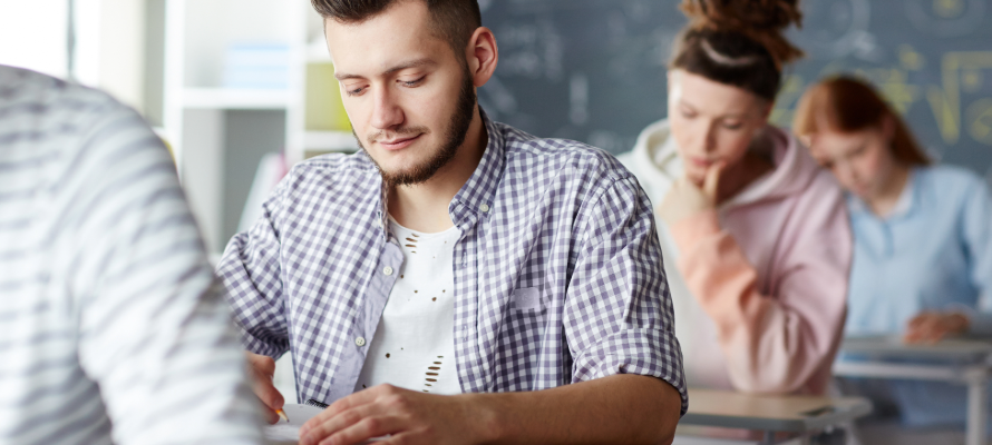 Drei Personen sitzen hintereinander an Schreibtischen und schreiben auf Papier oder lesen.