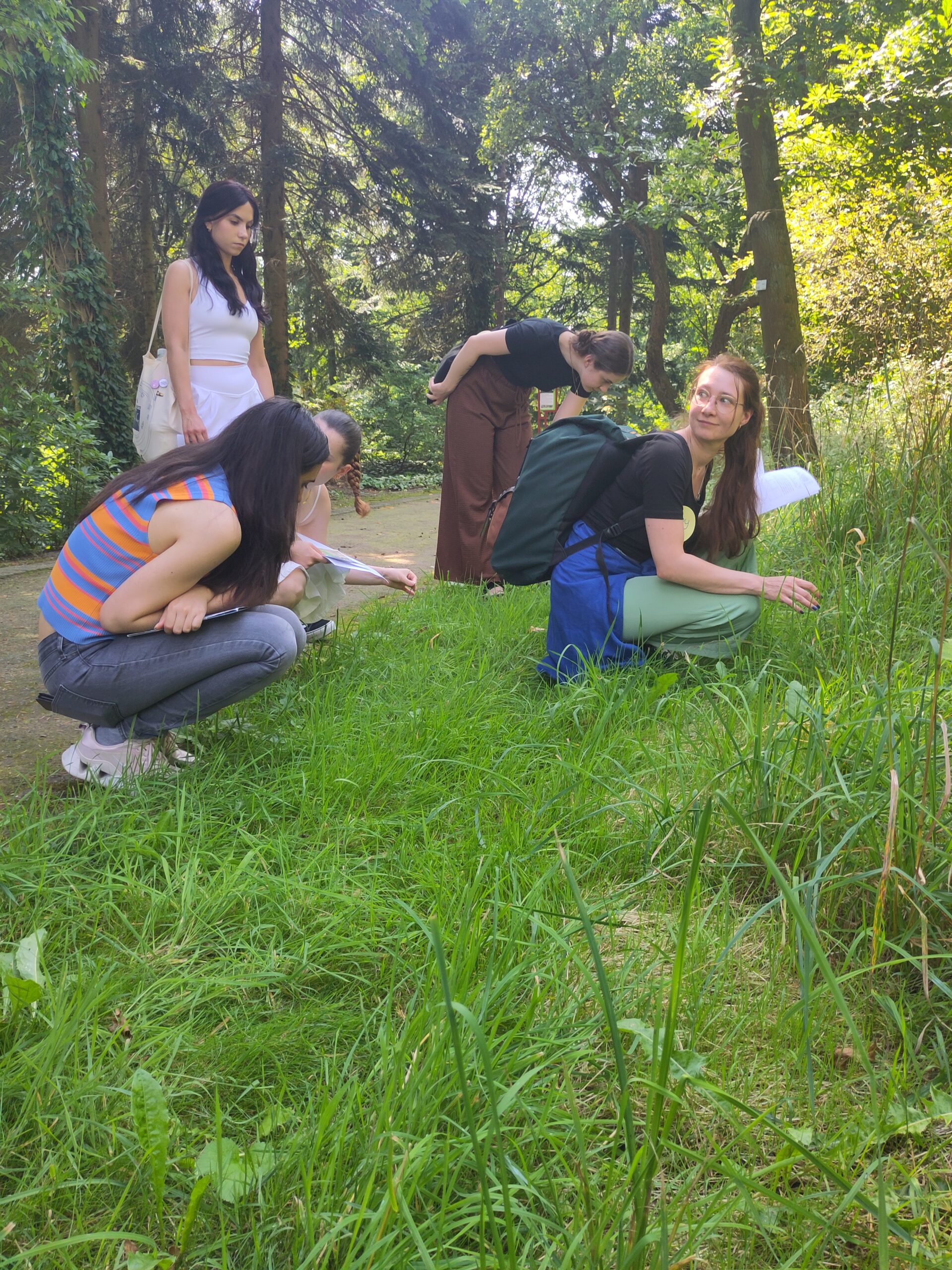 Fünf Personen in der Natur, vier davon hocken im Gras.