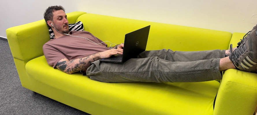 Mann liegt auf einem Sofa und schreibt auf einem Laptop